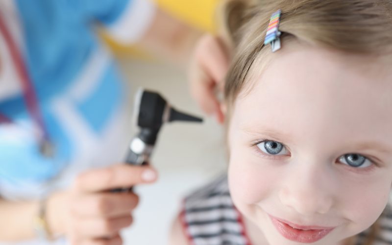 Doctor examining ear with otoscope for little smiling girl